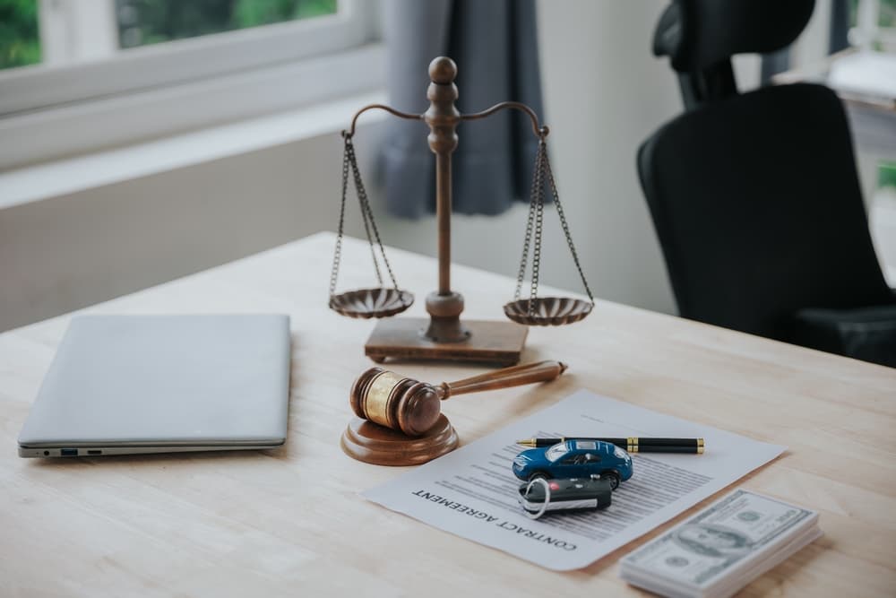 Law office desk with scales of justice, gavel, car key, and legal documents symbolizing car accident and injury law. Law office desk with scales of justice, gavel, car key, and legal documents symbolizing car accident and injury law.