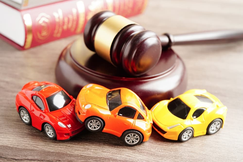 Toy cars involved in a mock car crash beside a judge’s gavel, symbolizing car accident law and legal claims.