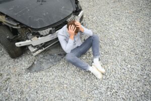 Young white man driver in car accident and holding his head near broken car on the road after a car accident.