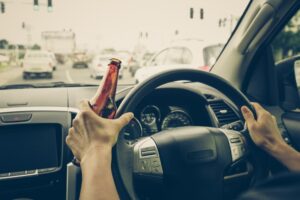 A man driving car while beer bottle in hand