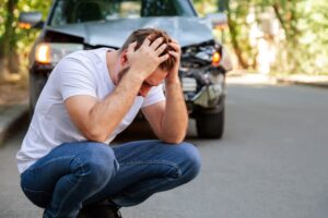 Young white man driver in car accident and holding his head near broken car on the road after a car accident.