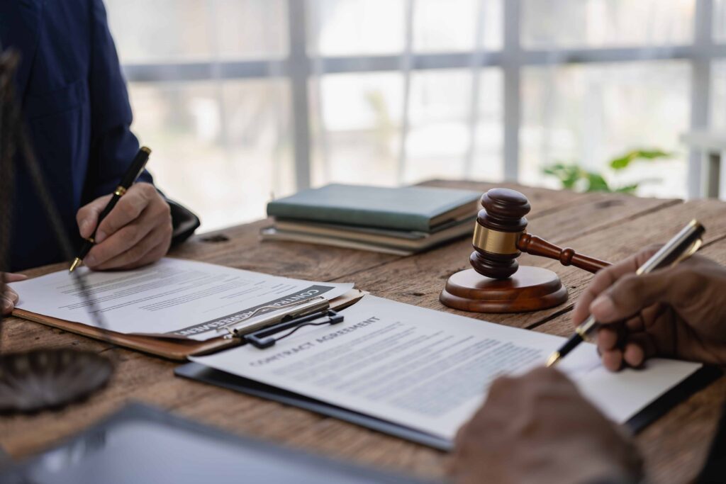 Lawyers reviewing and signing legal contract documents with a gavel on desk in law office. Lawyers reviewing and signing legal contract documents with a gavel on desk in law office.