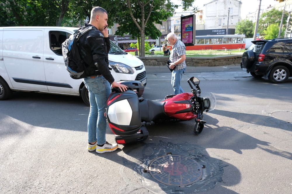 motorcyclist standing next to fallen bike after road accident