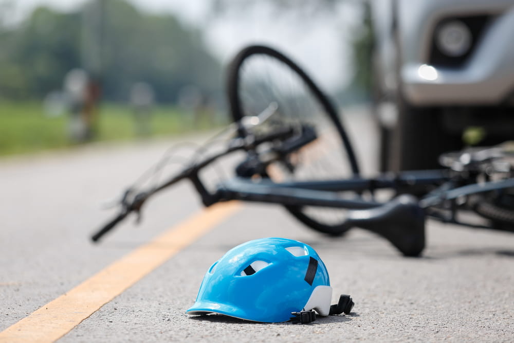 Bicycle helmet and damaged bicycle on the road near a vehicle after an accident, illustrating injury claims caused by negligence.