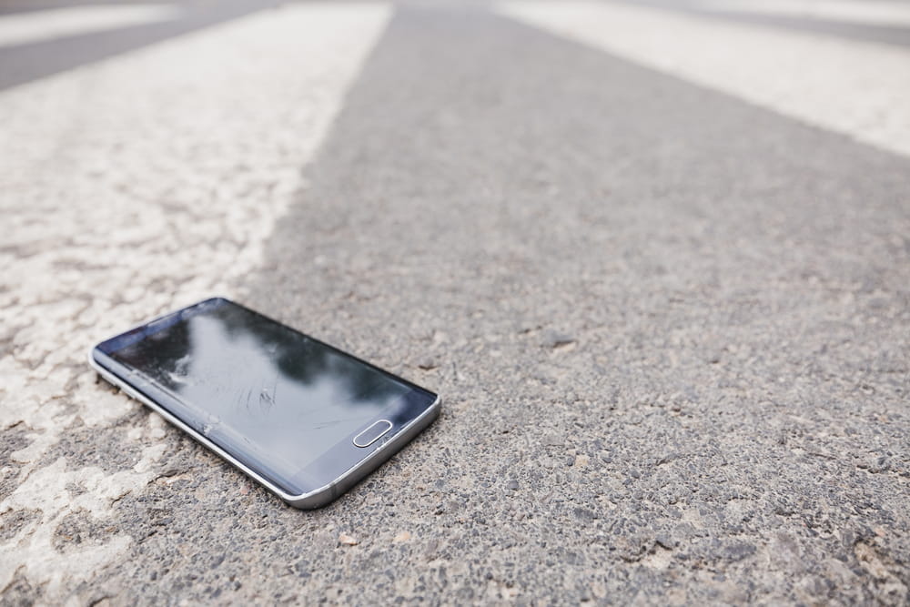 Cell phone lying on the pavement near a crosswalk after a pedestrian accident scene.