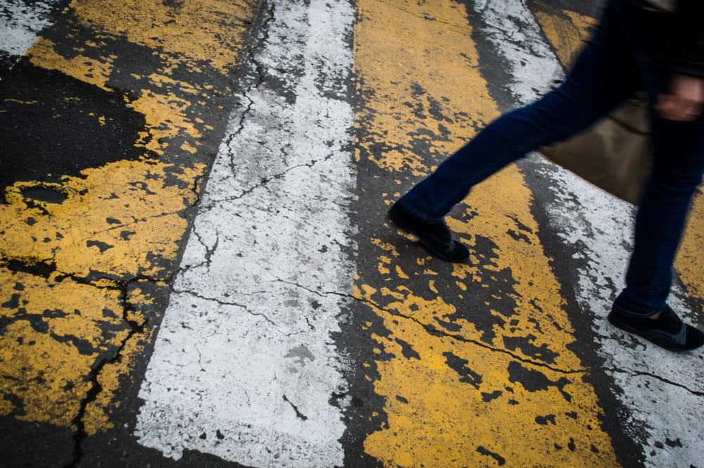 Pedestrian walking across worn crosswalk markings in a busy transit area, highlighting pedestrian safety concerns.