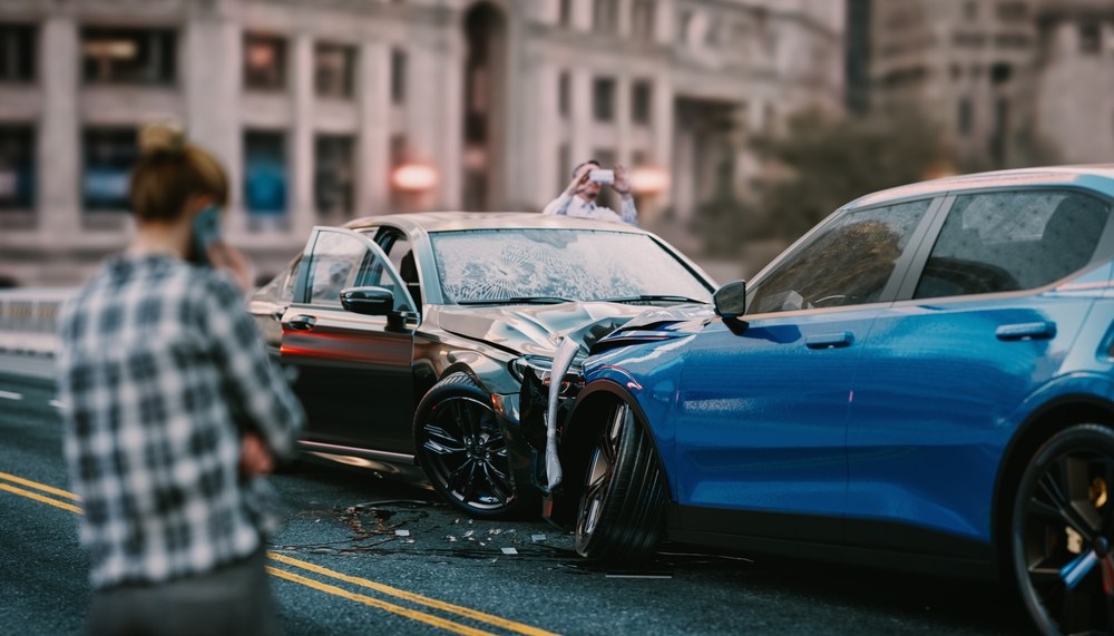 Person photographing a car accident scene with two damaged vehicles on the road