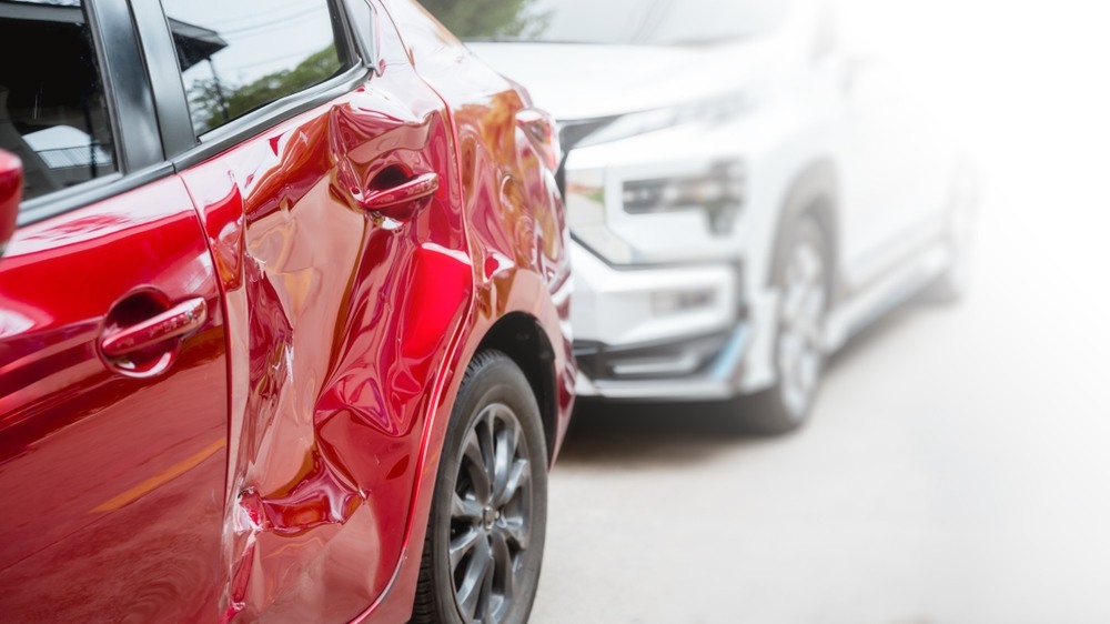 Red car with a dented rear door and quarter panel parked beside a white SUV after a collision
